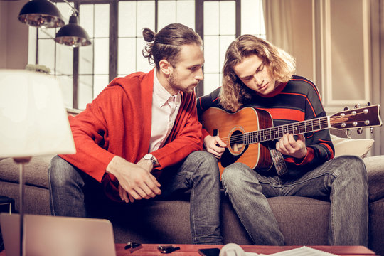 Bearded dark-haired guitar teacher listening to his student
