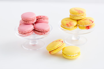 sweets, pastry and food concept - lemon yellow and pink macarons on glass confectionery stand over white background