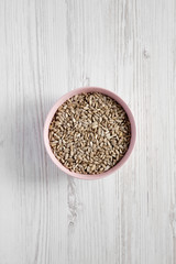 Hulled sunflower seeds in a pink bowl over white wooden surface, top view. Flat lay, overhead, from above.