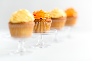 food, pastry and sweets concept - cupcakes with buttercream frosting on glass confectionery stand over white background