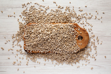 Hulled sunflower seeds on rustic wooden board over white wooden background, top view. Overhead,...