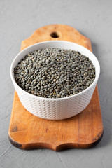 Dry green french lentils in gray bowl  over concrete surface, side view. Close-up.