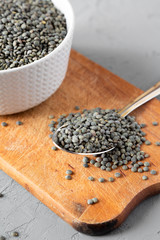 Dry green french lentils on rustic wooden board, side view. Close-up.