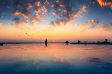 Romantischer Sonnenuntergang mit Spiegelung im Wasser eines Infinity Pools