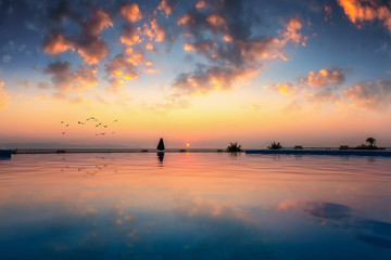 Fototapeta premium Romantischer Sonnenuntergang mit Spiegelung im Wasser eines Infinity Pools