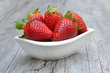 Fresh strawberries in ceramic white bowl on rustic wooden background.  Red, sweet berries.