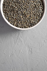 Dry green french lentils in a bowl over gray background, top view. Overhead, from above, flat lay. Copy space.