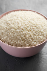Dry white rice basmati in a pink bowl over concrete background, side view. Close-up.