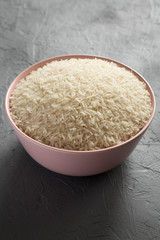 Dry white rice basmati in a pink bowl over gray background, side view. Closeup.