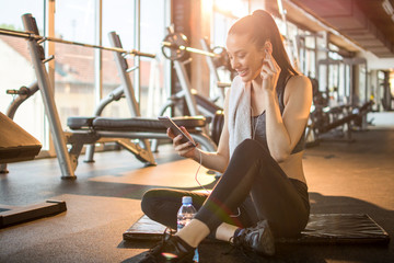 Beautiful young sportswoman with earphones listening to music on smart phone after sports training...