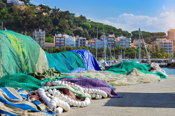 Empty green fishing net with floats lying on embankment of marine port. Industrial fishing in the summer season. Fishery for sea delicacies. Resort village Blanes, Spain, Costa Brava