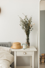 Soft home decor, small vases with wildflowers, straw hat, candle in  bedroom. White, pastel background 