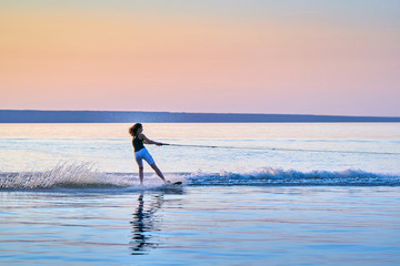 Woman surfer with black hair rolls on the board on a flat surface of water in the summer sunny evening.