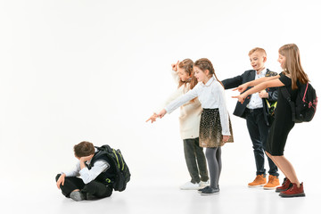 Little boy sitting alone on floor and suffering an act of bullying while children mocking in the...