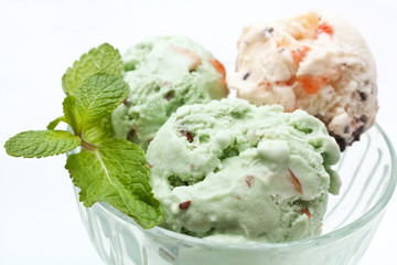 three scoops of pistachio and strawberry ice cream with mint leaves in a glass