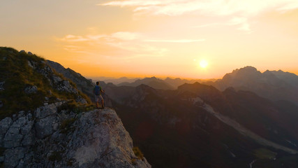 Obraz premium AERIAL Unrecognizable hiker stands on a cliff and observing the golden landscape