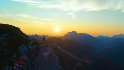 SILHOUETTE: Carefree hiker observes the picturesque sunset from a high cliff.