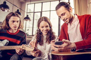 Beaming curly girl feeling joyful while learning to play guitar