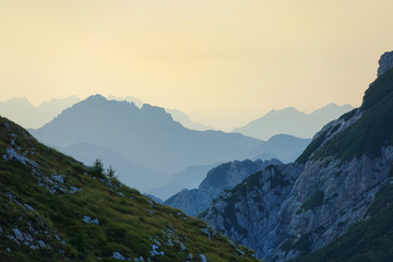 AERIAL: Flying over a steep grassy hill and towards mountaintops in the distance