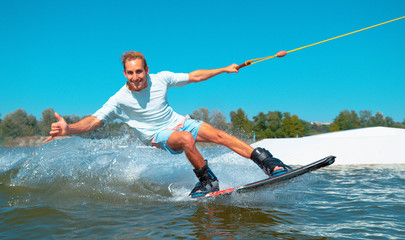 PORTRAIT: Cheerful wakeboarder gives the shaka sign while speeding past camera.