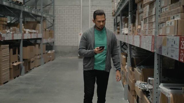 Man with a phone shopping at a warehouse store. Young man looking for goods on the shelves using smartphone. - Powered by Adobe