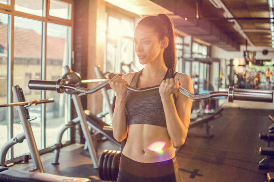 Fit sportswoman working out with curl bar in gym