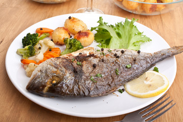 Roasted Sea Bream fish with vegetables on a white plate