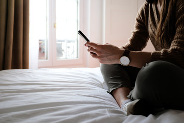 Frau sitzt auf ihrem Bett in der Wohnung und hat ein Handy in der Hand