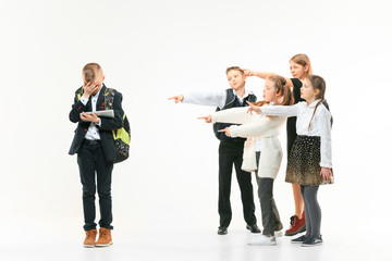 Little boy standing alone and suffering an act of bullying while children mocking in the...