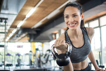 Fototapeta na wymiar Smiling young woman working out with kettle bell in gym