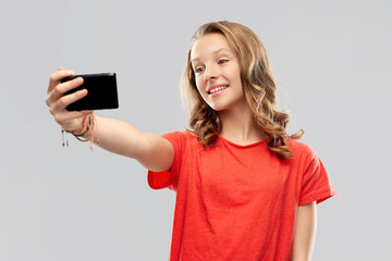 Fototapeta premium technology and people concept - smiling young woman or teenage girl in blank red t-shirt taking selfie by smartphone over grey background