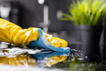 The girl washes the stove with a blue sponge in yellow gloves