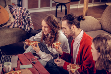 Curly teenage girl enjoying pizza break with her brothers at home