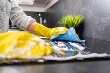 The girl washes the stove with a blue sponge in yellow gloves