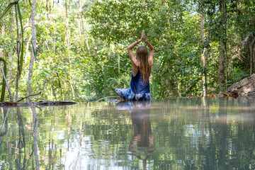 Fototapeta na wymiar Beautiful woman practicing yoga near turquoise water of cascade waterfall at deep tropical rain forest, island Koh Phangan, Thailand