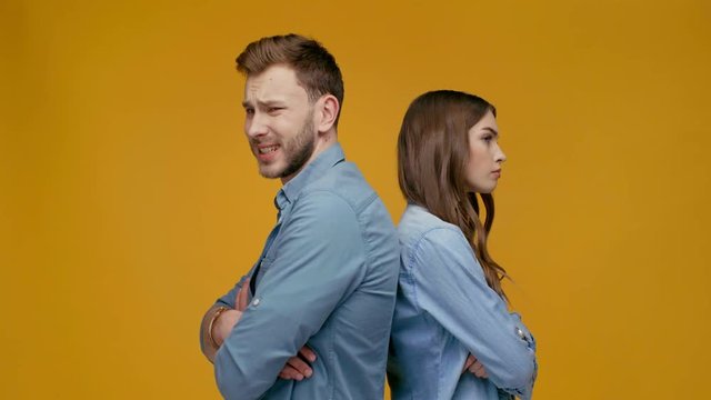 young couple standing back to back and man apologizing to woman after argument isolated on yellow