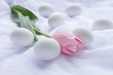 Fototapeta na wymiar White Easter eggs and pink tulip laying on white fresh linen