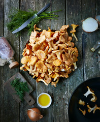 chanterelle mushrooms on a wooden table. A knife, a plate of mushrooms, fresh herbs and onions.