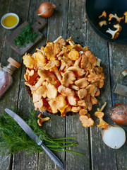 chanterelle mushrooms on a wooden table. A knife, a plate of mushrooms, fresh herbs and onions.