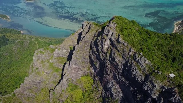 aerial shot of incredible landscape,rocky green mountain peak,with green trees near the beautiful blue ocean and strong sunlight.one of the best mauritius island can offer.filmed with drone 4K 30fps