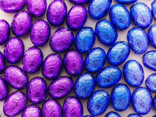 Colorful chocolate candy easter eggs wrapped in multicolored foil covering a table