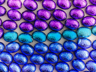 Colorful chocolate candy easter eggs wrapped in multicolored foil covering a table