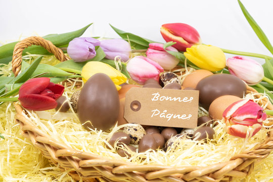 Joyeuses P&acirc;ques &eacute;crit en fran&ccedil;ais sur une &eacute;tiquette entour&eacute;e de tulipes pastel et diff&eacute;rents oeufs de P&acirc;ques