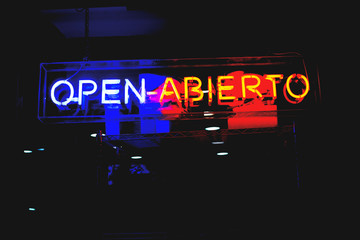 Neon shop "Open" (In Spanish and English) store sign at night in street with copy space