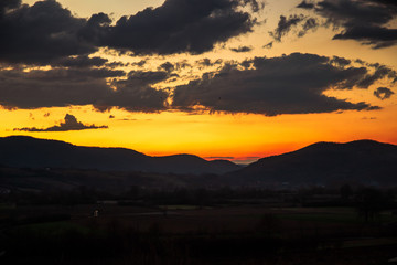 Beautiful colorful sunset with orange cloud sky. Rural landscape with hills and mountains.