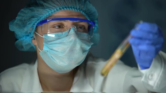 Vet lab assistant looking at meat sample in yellow liquid, swine flu analysis