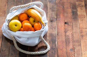 Close-up ecologic white linen bag of fruits on old wooden table.