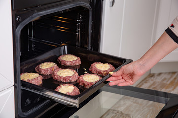 Woman hands putting baking tray with cutlets or meatballs and into oven