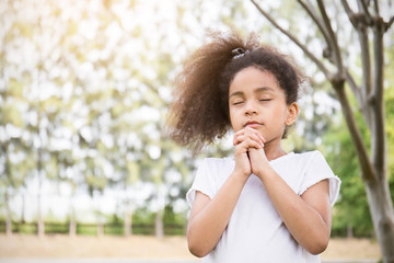 Portrait of little cute girl praying in the park, young girl with her hands together, closeup...