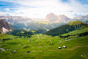 Fototapeta na wymiar peaceful view of a green valley full of wooden chalet and dolomites mountains over the horizon during summer in val gardena, saslong, south tyrol